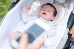 Schlfendes Baby, im Vordergrund hält eine Hand in Smartphone