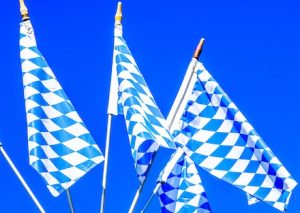 Mehrere Flaggen mit dem bayrischen blau-weißen Rautenmuster vor blauem Hintergrund.