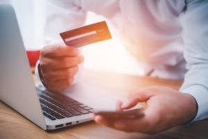 Hand mit Bezahlkarte und ein Laptop im Gegenlicht