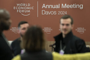 Unscharf abgebildete Personen vor einer braunen Wand mit dem Logo des Weltwirtschaftsgipfels Davos 2024.