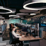 Das Bild zeigt das Innere des IT-Lagezentrums mit Personen an Bildschirmen und großen Monitoren an den Wänden.