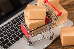 Symblbild: Miniatureinkaufswagen mit Kartons auf einer Laptop-Tastatur.