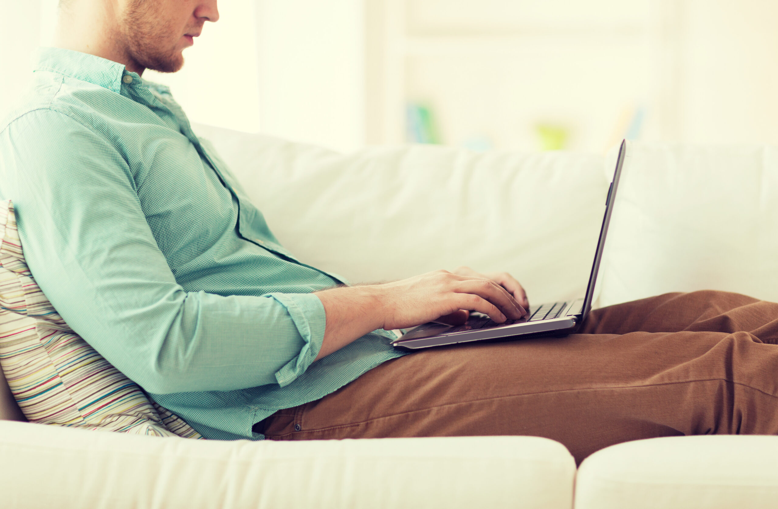 Mann sitzt auf einem Sofa und tippt auf seinem Laptop.