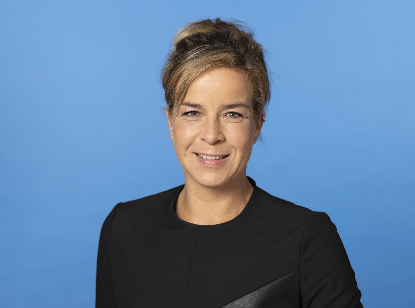 Poerträt der NRW-Wirtschaftsministerin Mona Neubaur vor blauem Hintergrund.