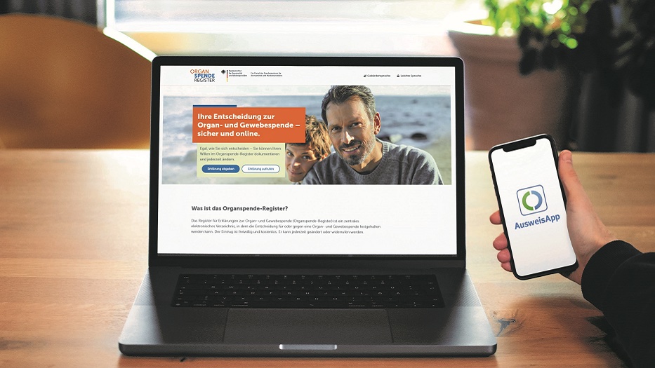 Zu sehen ist ein Laptop, der www.organspende-register.de zeigt, und daneben eine rechte Hand mit einem Smartphone, auf dem die AusweisApp geöffnet ist.