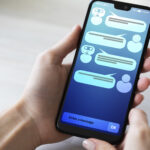 Hände halten Smartphone, auf dem Screen sieht man ein Chatprotokoll.