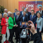 Gruppenbild der DMK-Teilnehmenden. Man sieht etwa 20 Personen in Business-Kleidung zusammenstehen, im Hintergrund Holzvertäfelung und DMK-Banner.