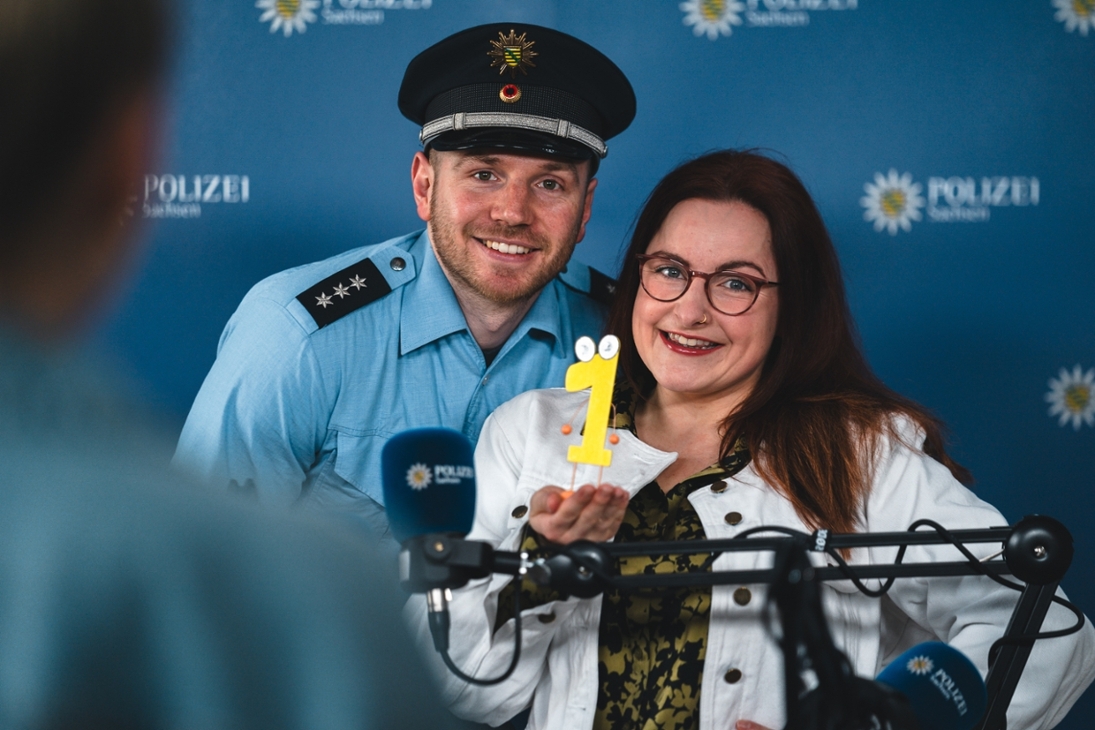 Ein Mann in Polizeiuniform und eine Frau stehen hinter einem Mikrofon.