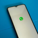 Ein Smartphone liegt schräg auf einer blauen Oberfläche. Der weiße Screen zeigt in der Mitte das WhatsApp-Logo