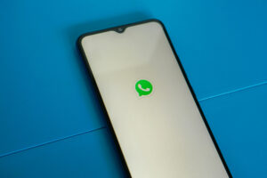 Ein Smartphone liegt schräg auf einer blauen Oberfläche. Der weiße Screen zeigt in der Mitte das WhatsApp-Logo