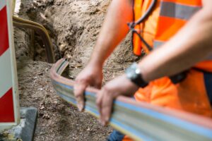 Das Bild zeigt eine Baustelle, auf der ein Arbeiter Glasfaserkabel verlegt.