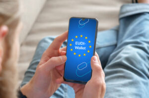 Blick über die Schulter einer Person, die ein Smartphone hält. Auf dem Screen ist das EUDI-Wallet-Logo.