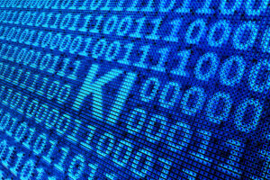 Verpixelte, in Blau gehaltene Ansicht eines Bildschirms, der neben zahlreichen Nullen und Einsen die Buchstaben "KI" zeigt.