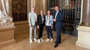 Vier Personen in sommerlicher Business-Garderobe stehen in einem historischen Saal.