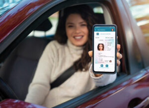 Eine junge Frau hält ihr Smartphone in die Kamera, auf dessen Bildschirm ihr Führerschein zu sehen ist.