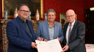 Im historischen Ambiente präsentieren Björn fecker, Claudia Plattner und Ulrich Mäurer gemeinsam eine Urkunde.
