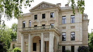 Blick auf die klassizistische Fassade einer Sandsteinvilla, umgeben von Bäumen (Sitz des BKG).