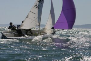 Glitzerndes Meer, darauf eine Jolle mit violettem Spinnaker.