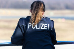 Rückansicht einer Polizistin in blauer Uniformjacke, darauf in weißer Schrift "Polizei".