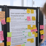 Blick auf Stellwände, die mit Stichpunkt-Listen und vielen bunten Post-Its beklebt sind.