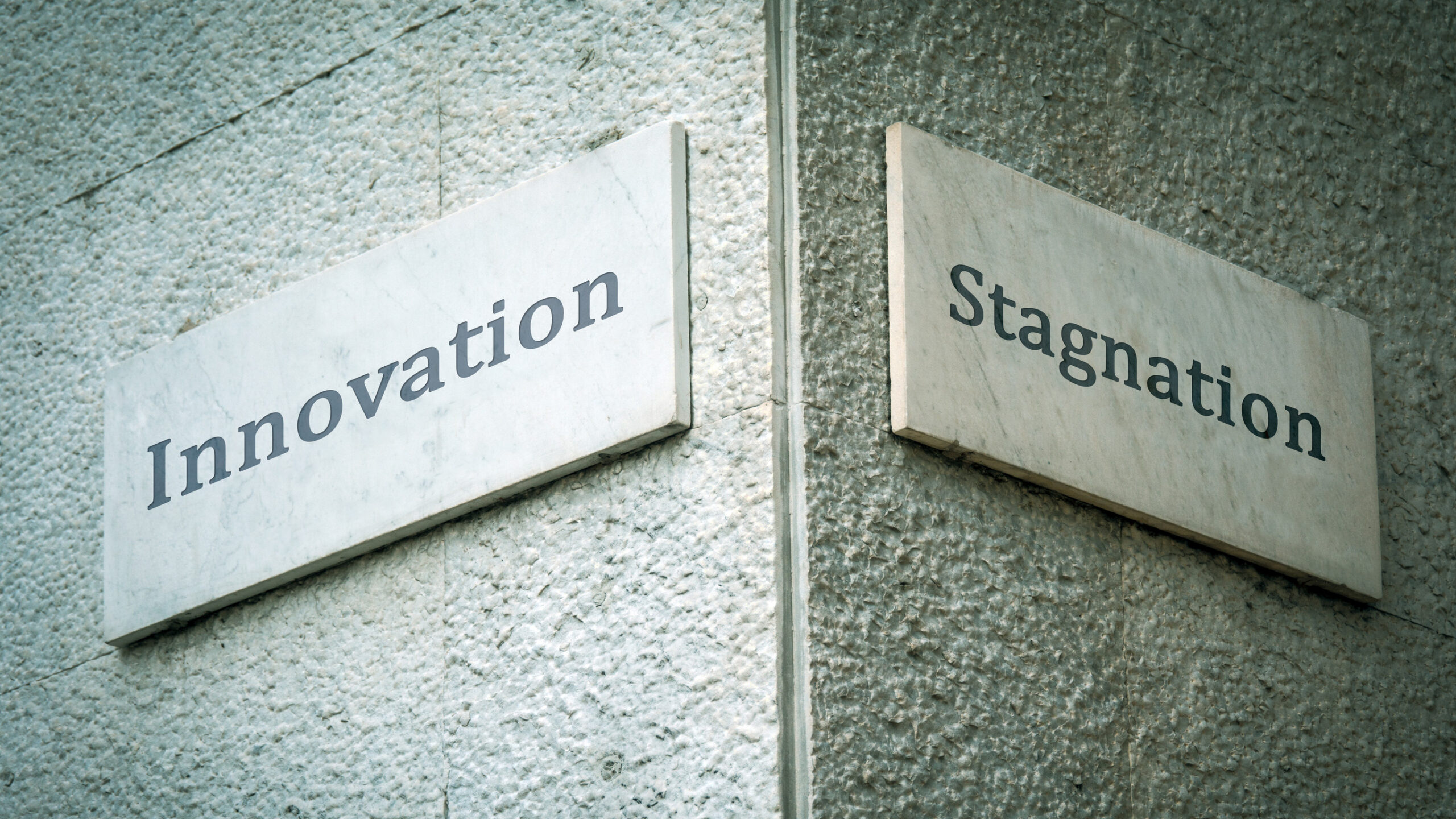 Hausecke mit zwei Straßenschildern, links "Innovation", rechts "Stagnation"