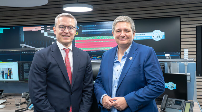 Bundesdigitalminister Dr. Karsten Wildberger und BSI-Präsidentin Claudia Plattner stehen vor einer Leinwand im Lagezentrum des BSI.