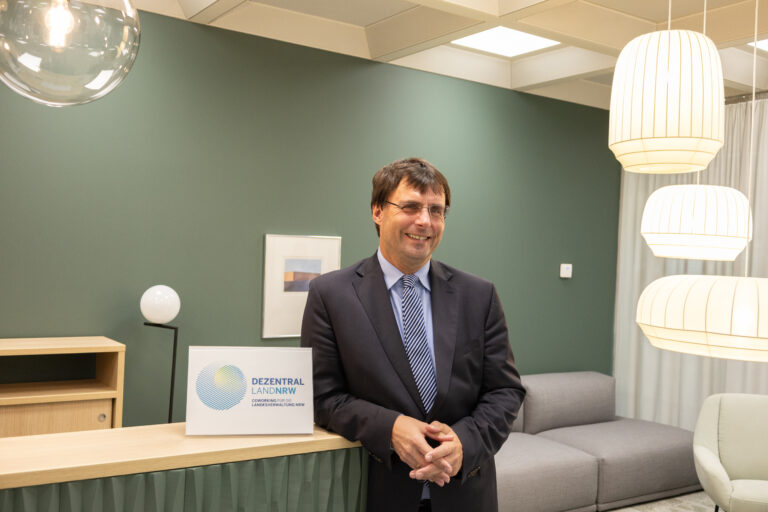 Finanzminister Optendrenk steht alleine in einem modern und freundlich eingerichteten Büroraum.