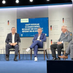 BSI-Chefin Claudia Plattner mit mehreren Männern in Anzügen auf einem Podium.