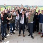 Gruppe aus rund 30, vorwiegend männlichen, Personen steht jubelnd auf einer Terrasse.