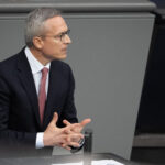 Bundesdigitalminister Karsten Wildberger mit dunklem Anzug im grauen Interieur des Bundestages, mit dynamischer Gestik.