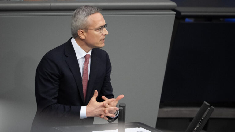 Bundesdigitalminister Karsten Wildberger mit dunklem Anzug im grauen Interieur des Bundestages, mit dynamischer Gestik.