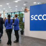 SCCON-Schriftzug im Eingangsbereich einer Halle, daneben steht eine Personengruppe.