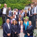 Gruppenbild der IT-Planungsrats-Mitglieder vor einer weinbewachsenen Fachwerk-Ziegel-Wand.