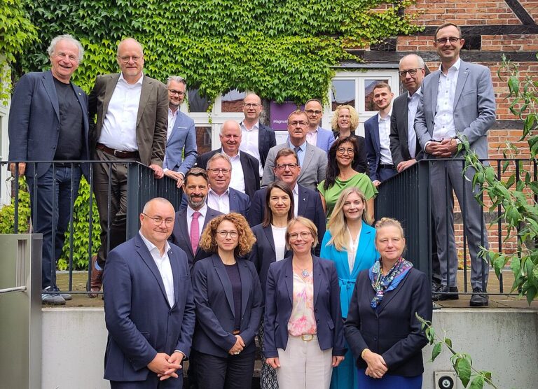 Gruppenbild der IT-Planungsrats-Mitglieder vor einer weinbewachsenen Fachwerk-Ziegel-Wand.
