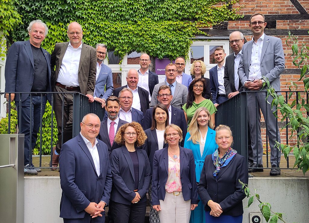 Gruppenbild der IT-Planungsrats-Mitglieder vor einer weinbewachsenen Fachwerk-Ziegel-Wand.