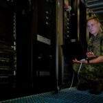 Ein Mann in Soldatenuniform kniet vor einem Serverrack.