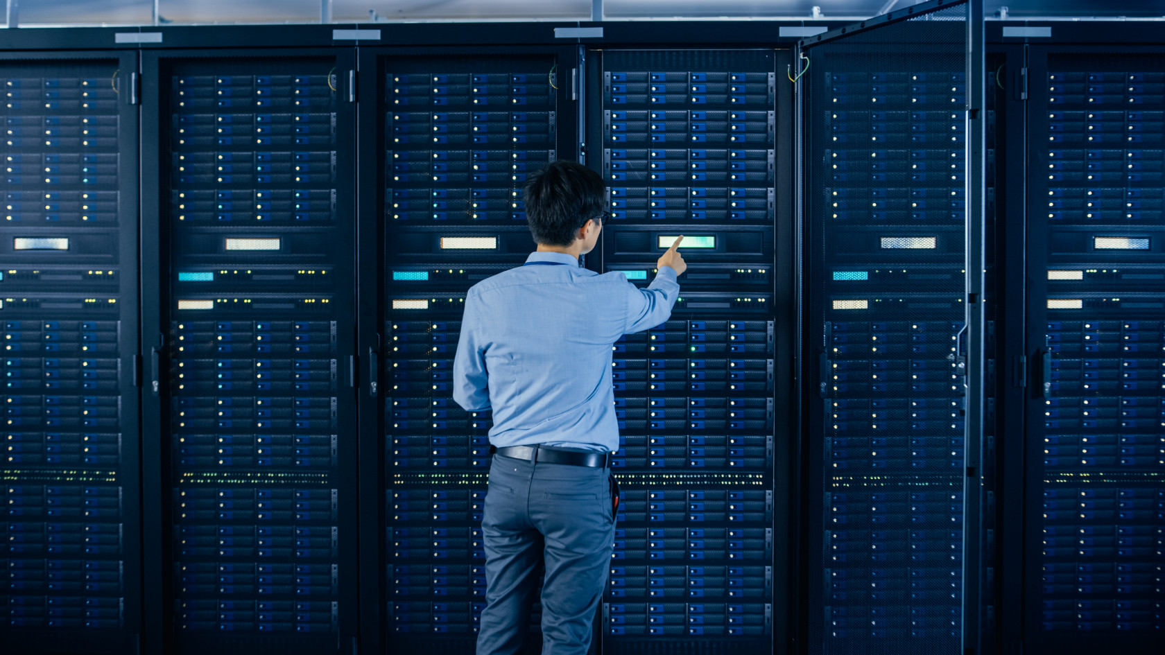 Rückenansicht eines Mannes vor einem Serverrack, die Szenerie ist in blaues Licht getaucht.