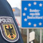 Wappen mit Aufschrift „Polizei“ auf Uniformärmel genäht. Im Hintergrund ein Schild „Bundesrepublik Deutschland“.