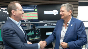 Innenminsietr Dobrindt und BSI-Chefin Plattner beim Handshake, im Hintergrund sieht man zahlreiche Monitore mit Grafiken und Statistiken sowie dem Logo "Nationales IT-Lagezentrum".