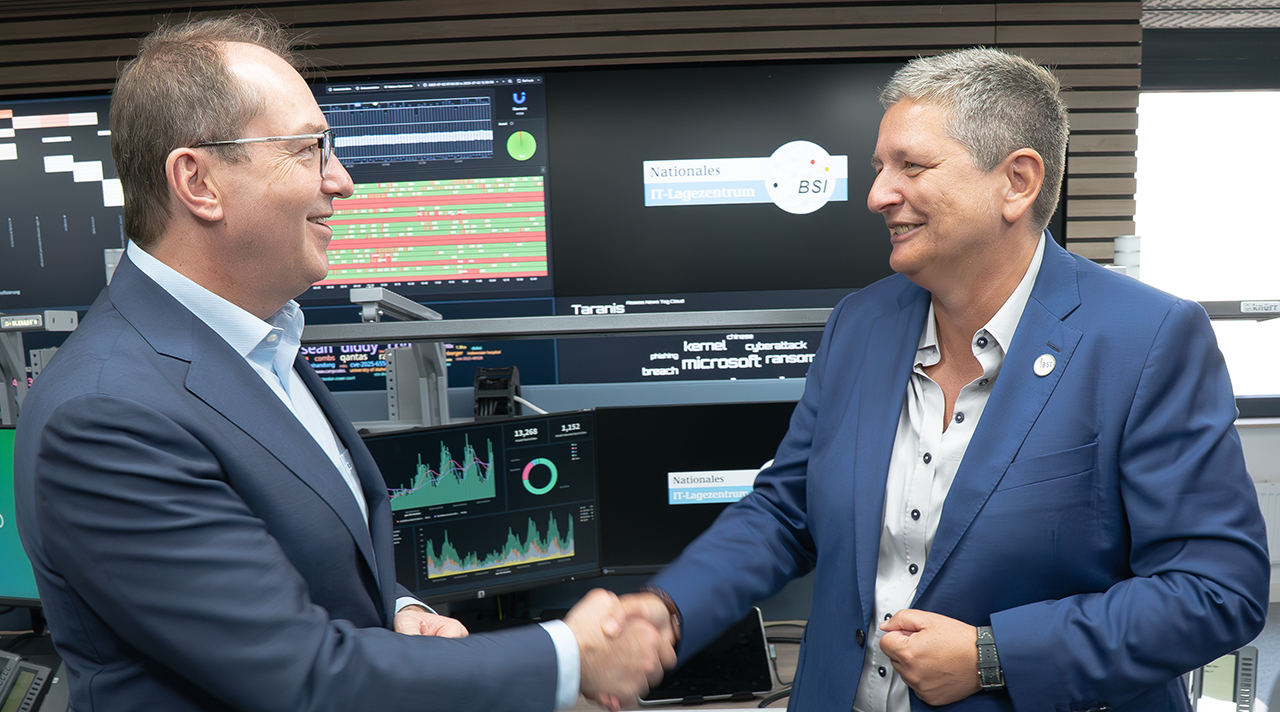 Innenminsietr Dobrindt und BSI-Chefin Plattner beim Handshake, im Hintergrund sieht man zahlreiche Monitore mit Grafiken und Statistiken sowie dem Logo "Nationales IT-Lagezentrum".