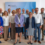 Gruppenfoto lächelnder, sommerlich gekleideter menschen Mvor einem BMDS-Aufsteller.
