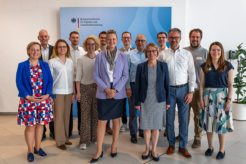 Gruppenfoto lächelnder, sommerlich gekleideter menschen Mvor einem BMDS-Aufsteller.
