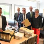 Wissenschaftsminister Timon Gremmels und weitere Personen stehen hinter einem Tisch mit Papierakten.