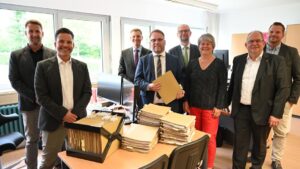 Wissenschaftsminister Timon Gremmels und weitere Personen stehen hinter einem Tisch mit Papierakten.