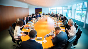Kabinettsitzung im Bundeskanzleramt - Mitglieder der Bundesregierung sitzen an einem ovalen Tisch vor einer holzvertäfelten Wand rechts und einer Fensterfront links.