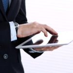 Close-up der Hände eines Mannes im Business-Anzug, der ein Tablet hält und bedient.