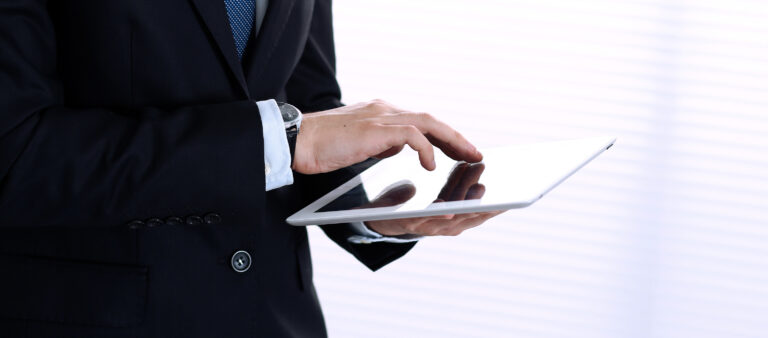 Close-up der Hände eines Mannes im Business-Anzug, der ein Tablet hält und bedient.