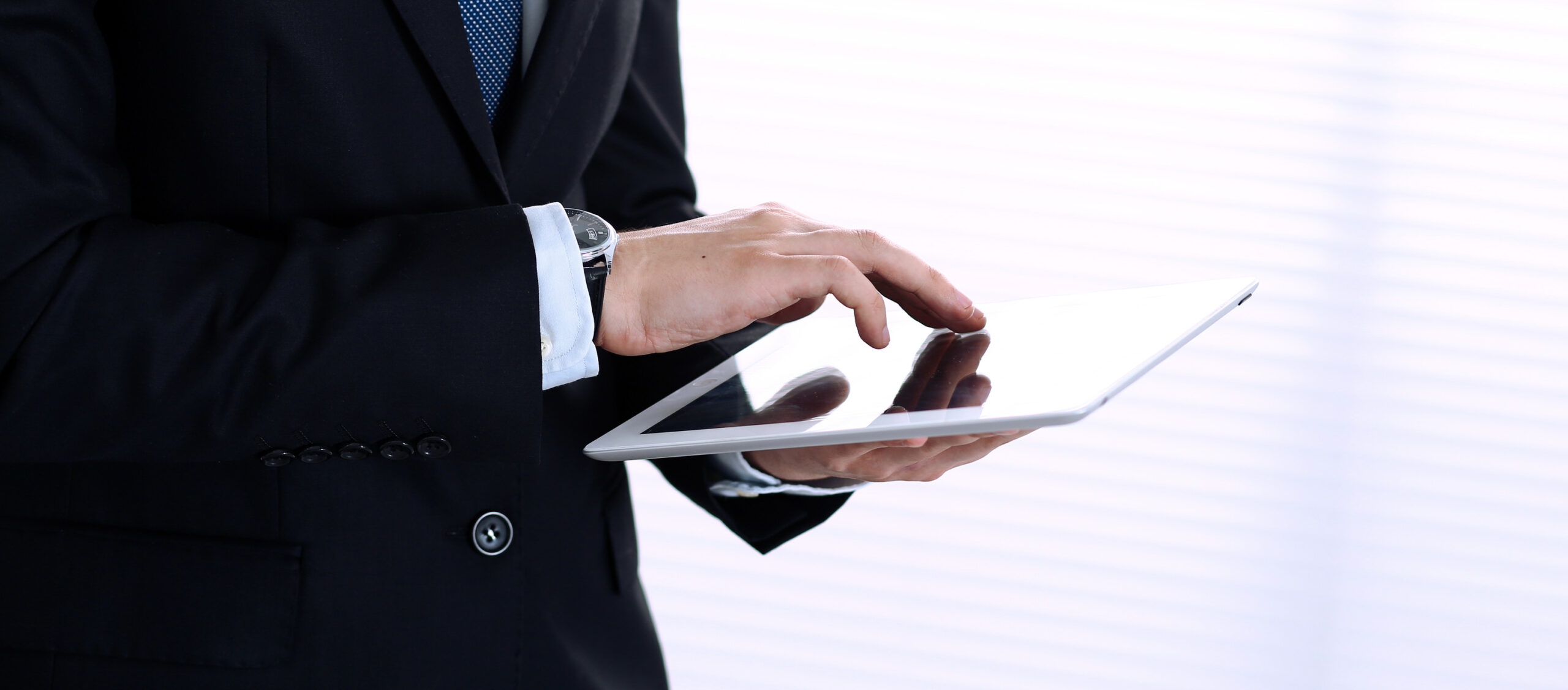 Close-up der Hände eines Mannes im Business-Anzug, der ein Tablet hält und bedient.