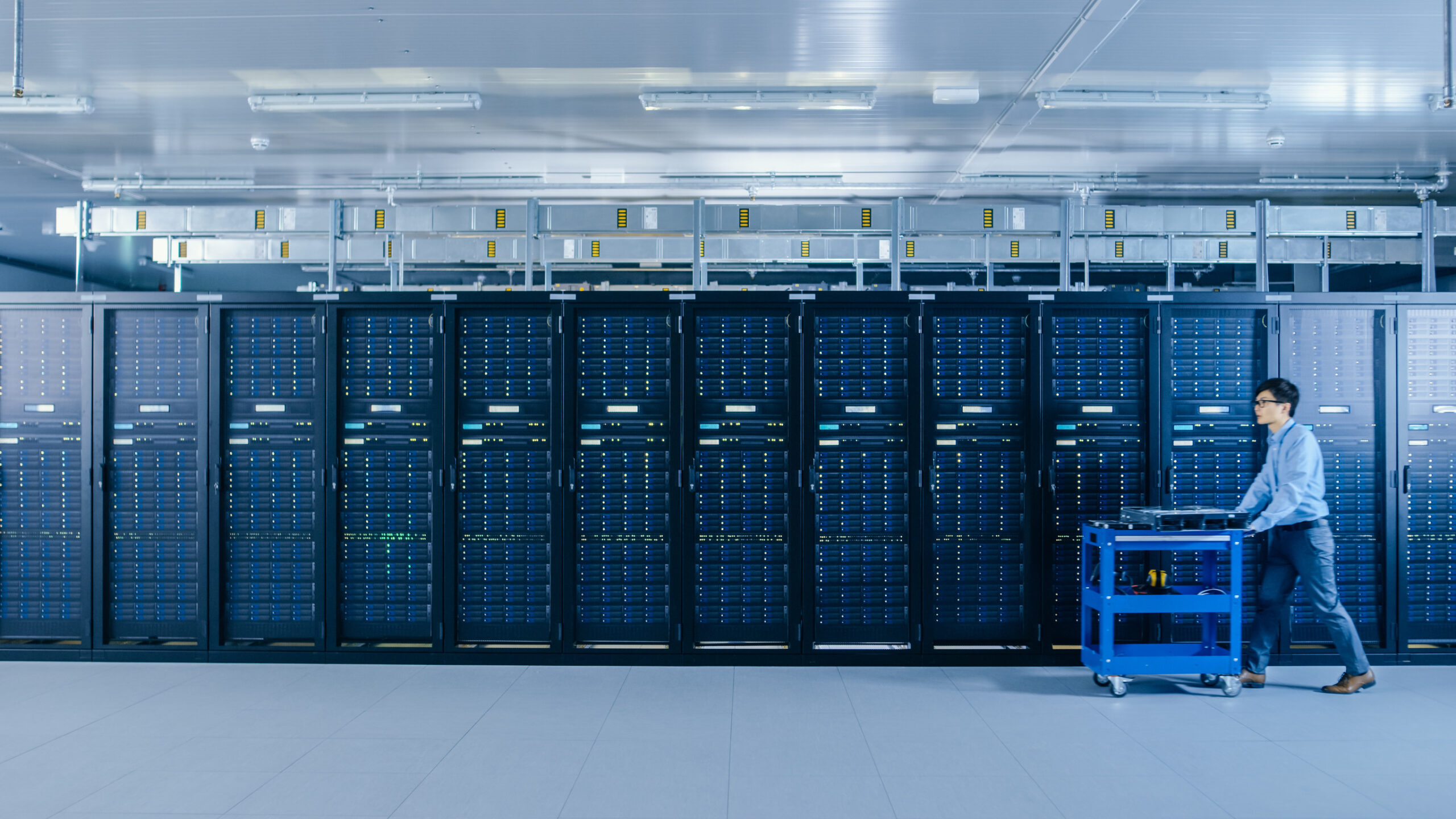 Modernes Rechenzentrum, ein IT-Techniker schiebt einen Wagen zwischen den Reihen der Server-Racks hindurch.