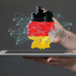 Composit: Hände halten ein Tablet, darüber schwebt ein 2D-Objekt mit den Umrissen und Farben von Deutschland, überlagert von einem gezeichneten Netzwerk.